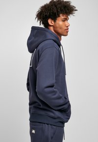Navy blue hoodie made of soft fabric, featuring a kangaroo pocket and adjustable drawstring. Includes a logo patch on the back.