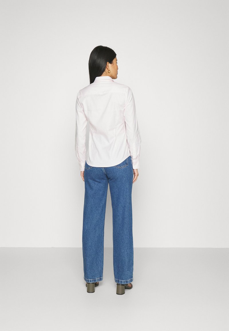 Chemise boutonnière rose clair à manches longues, associée à un jean en denim bleu ample. La chemise a un ourlet incurvé et le jean présente une coupe décontractée.