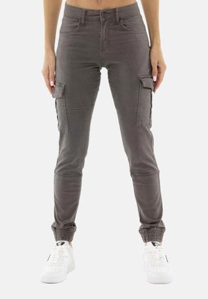 Pantalon cargo gris slim fit avec poches latérales et poignets élastiques porté avec des baskets blanches sur une personne debout.
