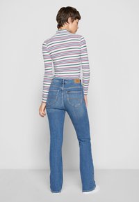 Top a rayas de manga larga con cuello alto, combinado con jeans acampanados azules que tienen bolsillos traseros y un parche de cuero con marca en la cintura.
