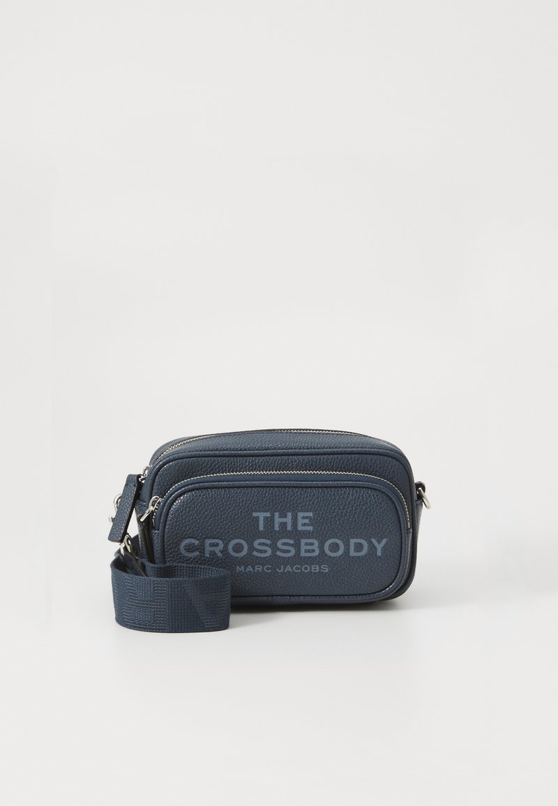 Kompakt navyblå læder crossbody taske med to lynlåslommer og justerbar rem, mærket "THE CROSSBODY MARC JACOBS" på fronten.