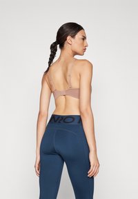 BH i lyse beige med justerbare stropper og krok bak, kombiniert med marineblå leggings med svart logo i livet. Glatt, tettsittende design.