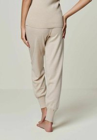 Beige Strickhose mit schmal zulaufenden Beinen, die eine glatte Textur und einen elastischen Bund aufweisen, von hinten mit barfuß abgebildet.