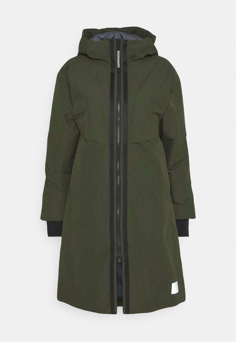 Vihreä takki, joka on valmistettu sileästä, vettä hylkivästä materiaalista ja jossa on vetoketjusuljenta sekä huppu. Varustettu kontrastivärisillä mustilla vetoketjuilla ja hihansuilla.