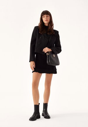 Black double-breasted cropped jacket, black fringed mini skirt, and black ankle boots, accessorized with a black handbag.