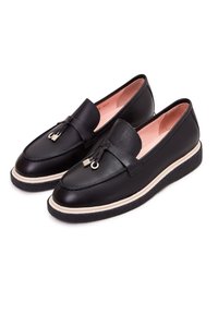 Mocassins en cuir noir avec semelles à bord crème, pompons décoratifs avec accents métalliques et doublure intérieure rose, présentés côte à côte sur fond blanc.