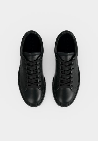 Ζευγάρι μαύρα δερμάτινα sneakers με κορδόνια και ανάγλυφες σόλες, φωτογραφημένα από πάνω σε λευκό φόντο.
