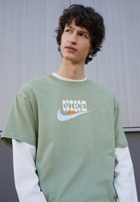 T-shirt en coton vert avec un col rond et des manches courtes, arborant un logo Nike coloré et le texte "NICE" dans une police ludique.