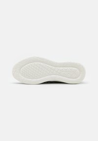 Zapatilla negra con una suela de goma blanca texturizada, que presenta un diseño de agarre con patrones y un logo en relieve en la parte inferior.