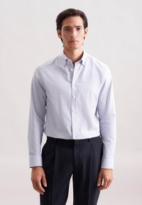 Koszula zapinana na guziki z białym tłem, niebiesko-błękitnym wzorem w kratkę, długimi rękawami i kieszonką z przodu. W zestawie z ciemnymi spodniami.