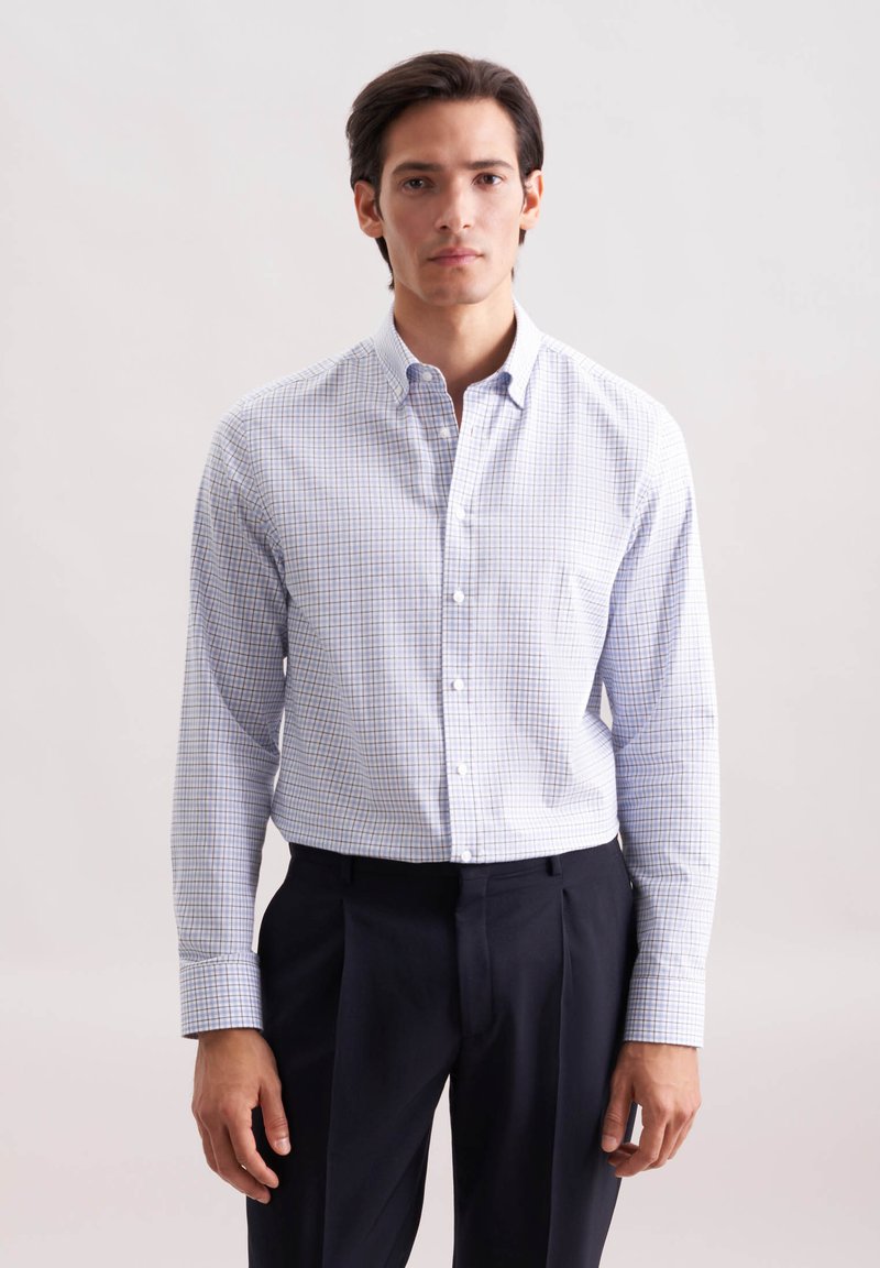 Koszula zapinana na guziki z białym tłem, niebiesko-błękitnym wzorem w kratkę, długimi rękawami i kieszonką z przodu. W zestawie z ciemnymi spodniami.