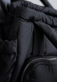 Svart dunsekk med quiltet design, som har glatt stoff, polstrede seksjoner og en sølvglidelås langs siden for lukking.