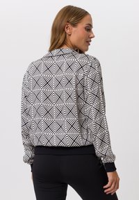 Schwarz-weiße Bomberjacke mit geometrischem Muster, gerippten Bündchen und Kragen. Glattes Gewebe mit lässiger Passform.