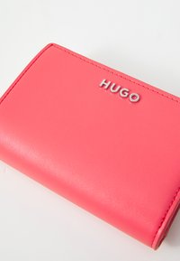 Portafoglio in pelle rosa con texture liscia e bordi cuciti, caratterizzato dal logo argento "HUGO" ben visibile sulla parte frontale.