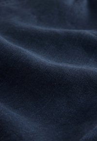 Dunkelblauer Marine-Stoff mit einer glatten, leicht strukturierten Oberfläche, die subtile Falten und Lichtvariationen im Material zeigt.