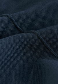Tissu texturé bleu marine foncé avec un motif tricoté, présentant des vagues et des plis subtils créant de la profondeur et de la dimension.