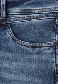 Jeans de mezclilla azul claro con una sutil textura desgastada, que cuentan con un bolsillo frontal, costuras visibles y un acento de botón metálico.