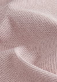 Nahaufnahme eines weichen, blassrosa gestrickten Stoffes mit feinen, gleichmäßigen Maschen und sanften Falten, die subtile Schatten erzeugen.