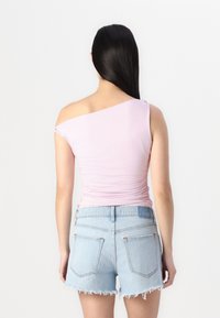 Top rosa claro de un solo hombro con detalle fruncido en el lateral, combinado con unos shorts de denim azul con dobladillo deshilachado. Textura suave, diseño ajustado.