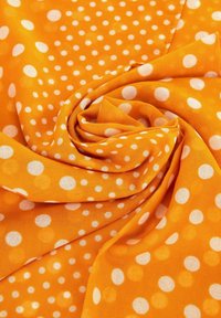 Tela naranja con puntos blancos, que muestra una textura ligera y suave, dispuesta en un patrón espiral para enfatizar el diseño.