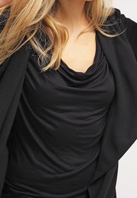 Černý top s kapucí vyrobený z hladké, lehké tkaniny, se záhybovým detailem a vrstveným designem pro splývavý siluetu.