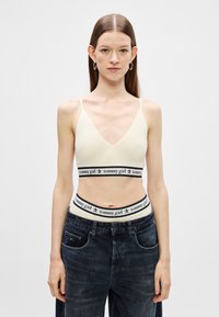 Ivory rebrovaný bralet s hlbokým dekoltom a úzkymi ramienkami. Obsahuje čierny pás so siluetou "tommy girl" a červenými hviezdami.