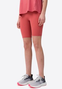 Pantalones cortos deportivos rojos con una textura suave, combinados con una camiseta rosa de corte holgado, complementados con zapatillas deportivas grises y rosas.