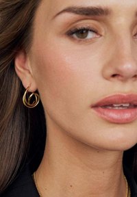 Guldiga hoops örhängen vrider sig i en spiraldesign. Ytan är slät och reflekterar ljus, med en minimalistisk estetik.