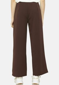 Un pantalon large marron avec une texture lisse et des plis à la taille, associé à des baskets blanches pour le contraste.