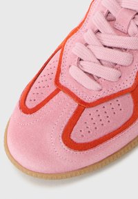 Sapatilhas de camurça rosa com realces em camurça laranja e detalhes perfurados. Apresentam uma língua em tecido rosa e sola de borracha texturizada.
