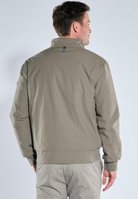 Khaki jacket with a high collar, designed with a boxy shape and smooth texture. Details include side seams and elastic cuffs at the wrists.