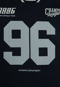 Camiseta de algodón negra con números perforados en blanco "96" y el texto "1996 EQUIPO IMPARABLE". Presenta "DEPARTAMENTO DE CORRER" debajo en blanco.