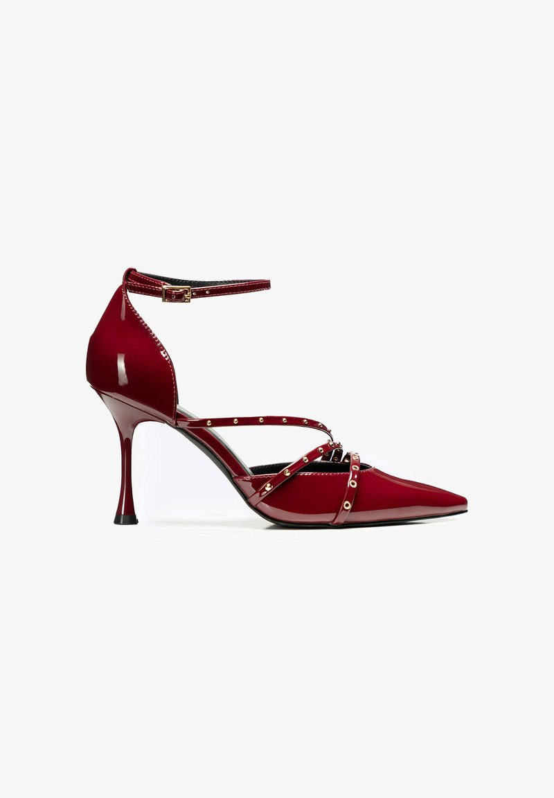 Scarpa con tacco alto in pelle lucida rossa, punta affusolata, cinturino alla caviglia, dettagli in metallo dorato e tacco a spillo curvo.