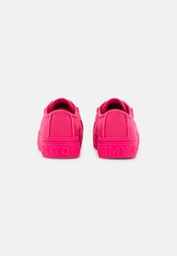 Zapatillas de lona rosa con una suela de goma texturizada, que presentan el "TOMMY" en relieve en la parte trasera y un diseño simple y de perfil bajo.