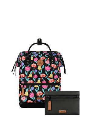 Schwarzer Rucksack mit buntem Blumenmuster und Lederakzenten neben einem kleinen schwarzen Reißverschlusstäschchen mit Lederdetails, beide mit CABAIA-Logo.