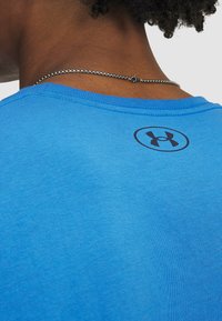 Camiseta de algodón azul con cuello redondo y mangas cortas, con un logo negro en la parte posterior. Textura suave y corte estándar.