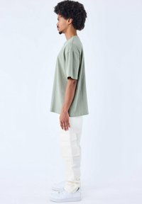 Lichtgroen oversized t-shirt van zachte stof, gecombineerd met crèmekleurige cargobroek met grote zijzakken en witte sneakers.