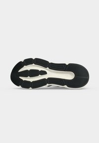 Semelle d'une chaussure de sport noire et blanche avec des motifs texturés conçus pour l'adhérence et le soutien sur un fond clair uni.