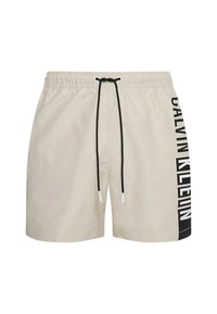 Pantaloni da bagno beige con vita regolabile, accessori neri e grande logo nero "CALVIN KLEIN" stampato verticalmente sul lato.