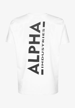Bijela pamučna majica s velikim crnim vertikalnim printom riječi "ALPHA" i "INDUSTRIES." Kratki rukavi i dizajn s okruglim izrezom.