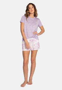 Camiseta corta de manga corta en color púrpura combinada con pantalones cortos blancos que presentan un patrón abstracto en rosa, fabricada en tejido ligero y de corte relajado.