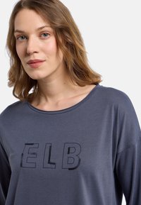 Dunkelgraues Langarmshirt mit den Buchstaben "ELB" aus schwarzen Pailletten. Weicher Stoff, weit ausgeschnittener Kragen, lockere Passform mit fallenden Schultern.