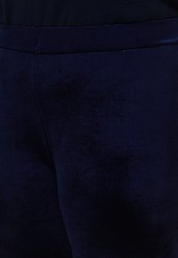 Βελούδινο παντελόνι σε ναυτικό μπλε χρώμα με ομαλή υφή, διαθέτει απλή μέση χωρίς ορατές τσέπες ή διακοσμητικά στοιχεία.