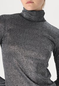 Garā piedurkņu turtlenecks tops metāliski melnā audumā, ar cieši pieguļošu dizainu, mīkstu tekstūru un smalku spīdumu.