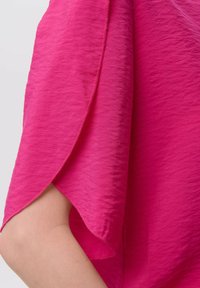Blusa fucsia con un acabado texturizado, que presenta mangas cortas drapeadas y una tela visiblemente suave y ligera.