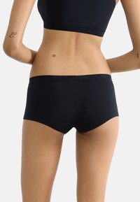 Mustat puuvillaiset poikashortsit, joissa on istuva muotoilu, pehmeä joustovyötärö ja sileä pinta. Minimalistinen brändäys vyötäröllä.
