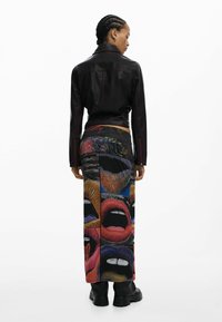 Must nahast jakk punaste õmblustega, mida kannab grafikaga seelik, kus on värvikirevad huulekujundid ja julged mustrid, kombineeritud massiivsete mustade saapadega.