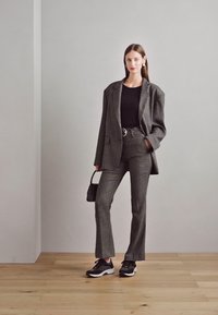 Gray checkered blazer with a matching pant and a black top, paired with black sneakers. The model holds a small black handbag.