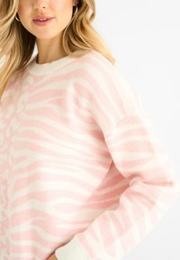 Jasnoróżowy sweter w białe paski zebry, miękka tekstura, okrągły dekolt i ściągacze. Luźny krój i oversize'owy fason.