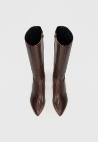 Botine maro, cu model de șarpe, până la genunchi, cu vârfuri ascuțite și închidere cu fermoar la spate. Textură netedă, cu un design ajustat.